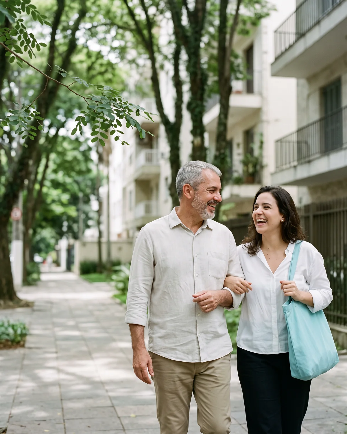 Pai e filha caminham de braços dados por uma rua arborizada, rindo juntos